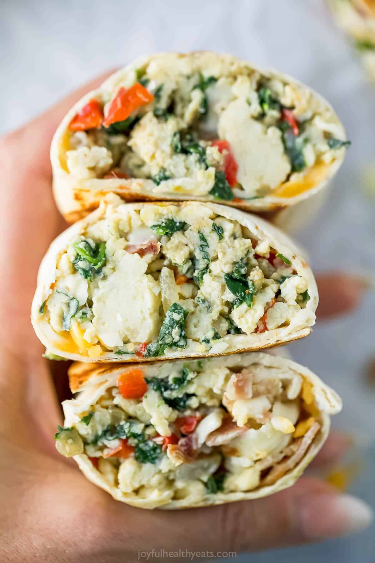 Hand holding 3 freezer breakfast burrito halves.