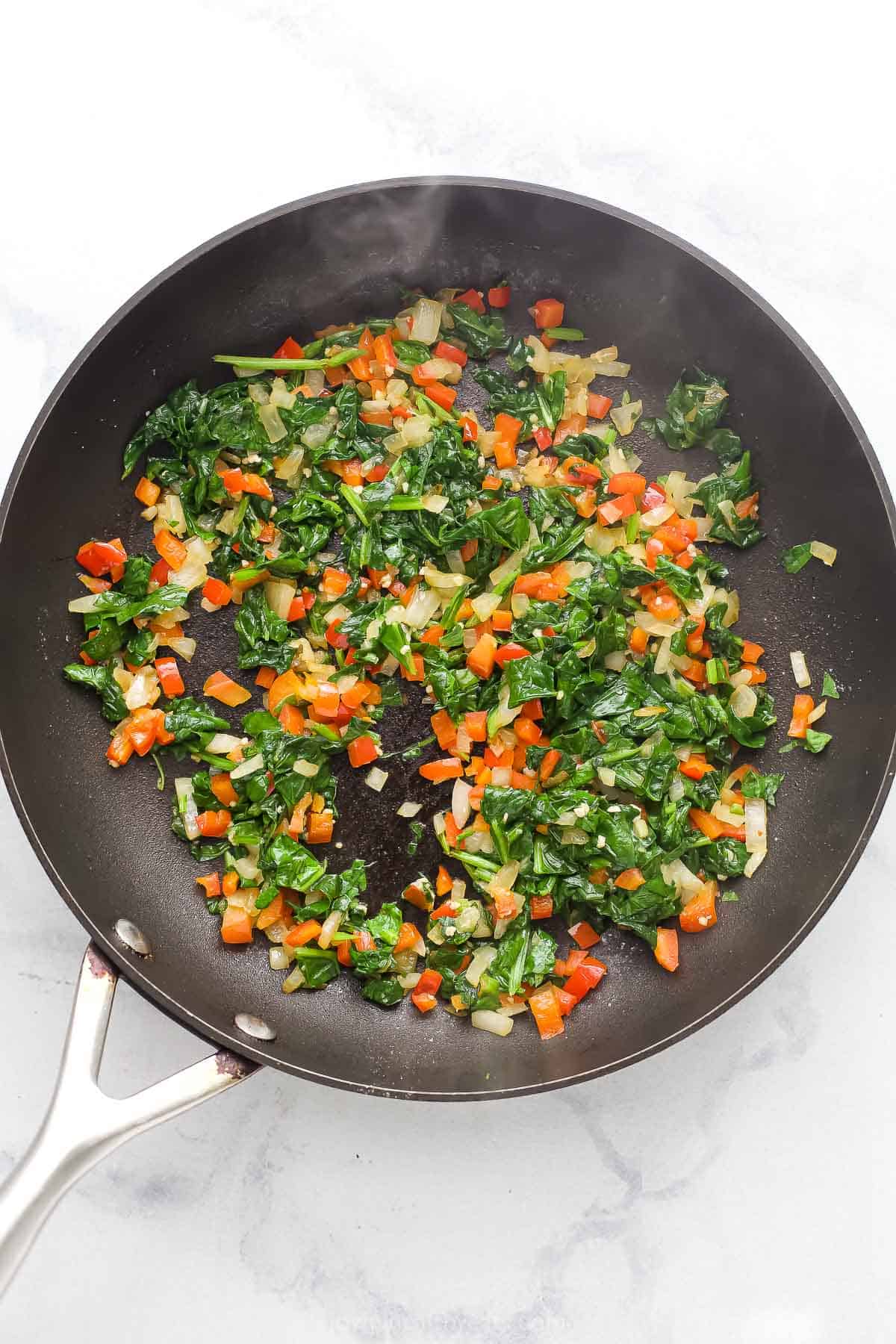 Spinach, onions, and red pepper in skillet.