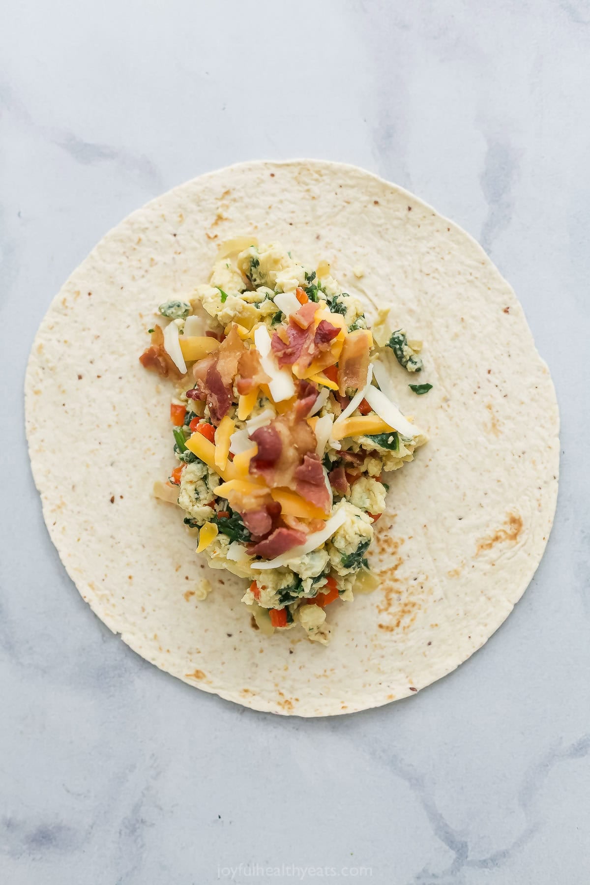 Scrambled eggs, veggies, cheese, and bacon added to tortilla.