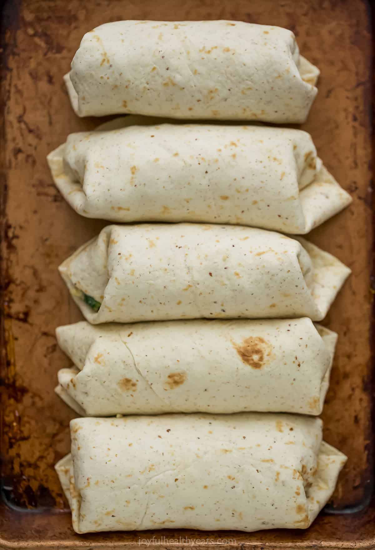 Freezer breakfast burritos lined up on sheet pan.