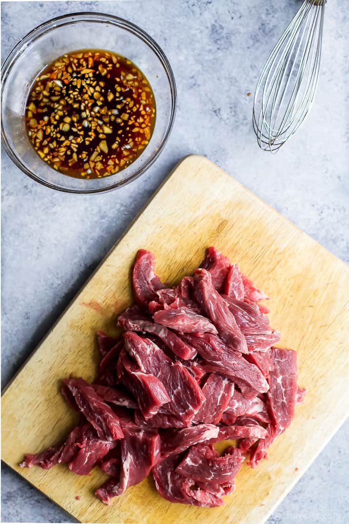 Raw sliced beef on a cutting board next to a bowl of sweet spicy korean sauce