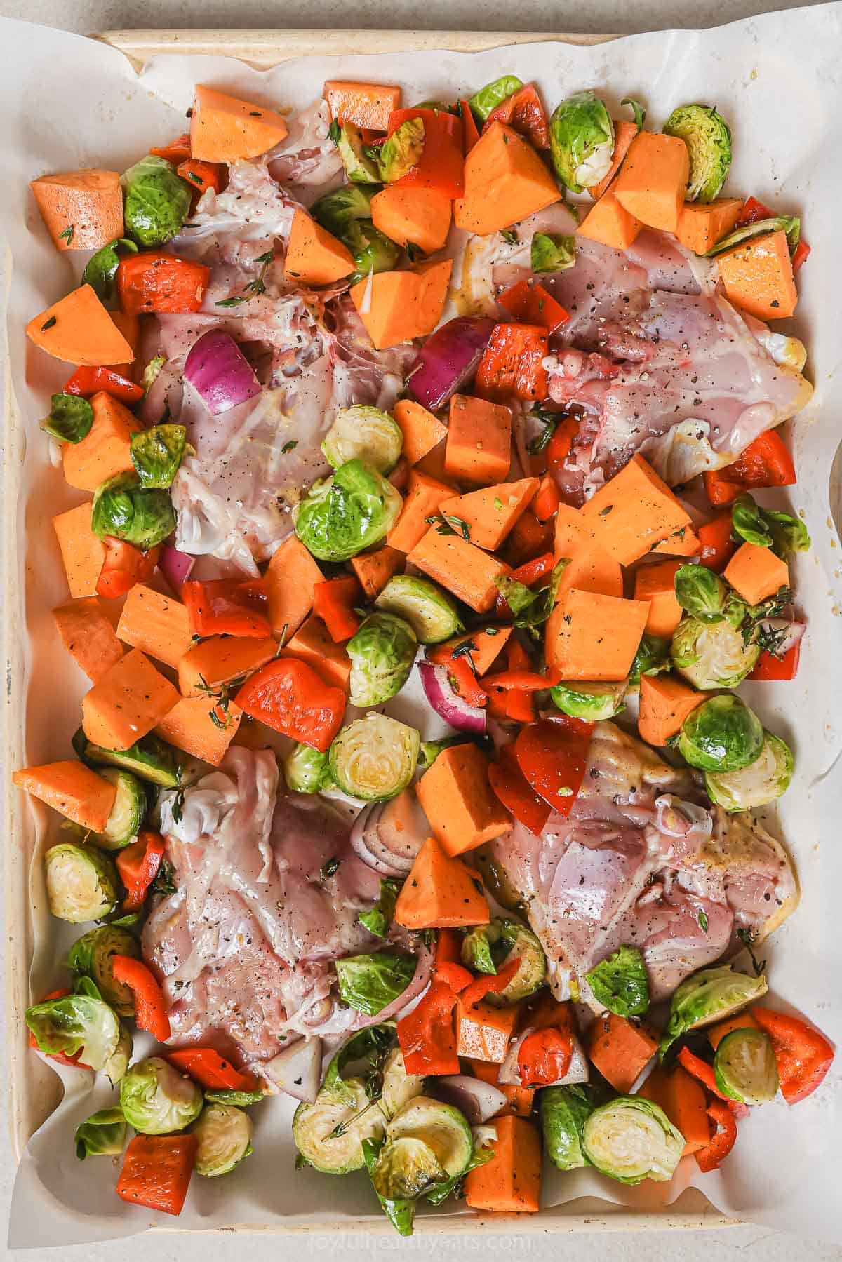 Veggies and raw chicken on the baking sheet. 