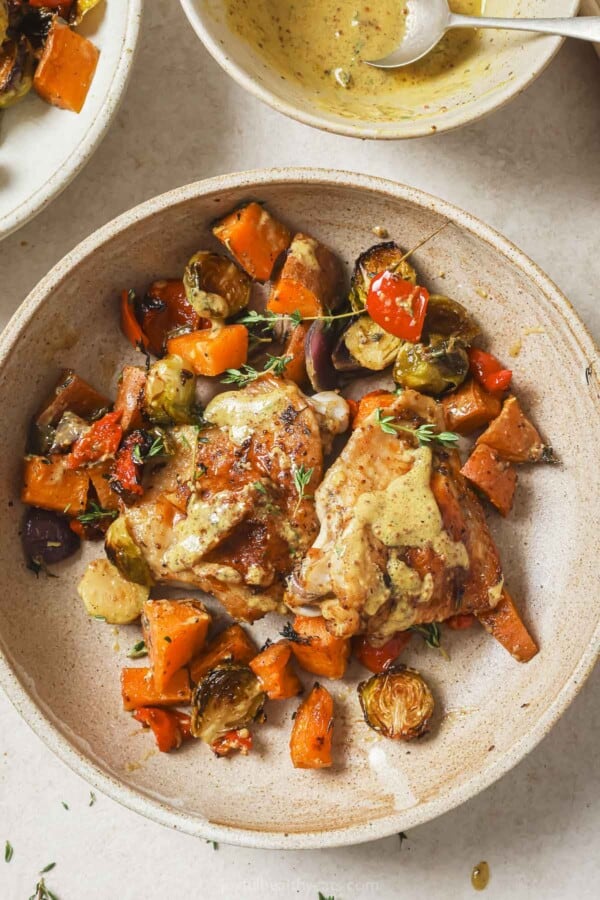 Sheet pan chicken thighs served with roasted veggies on a plate.