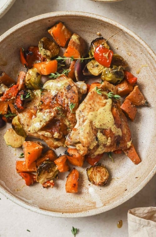 Sheet pan chicken thighs with extra honey mustard sauce in a bowl.