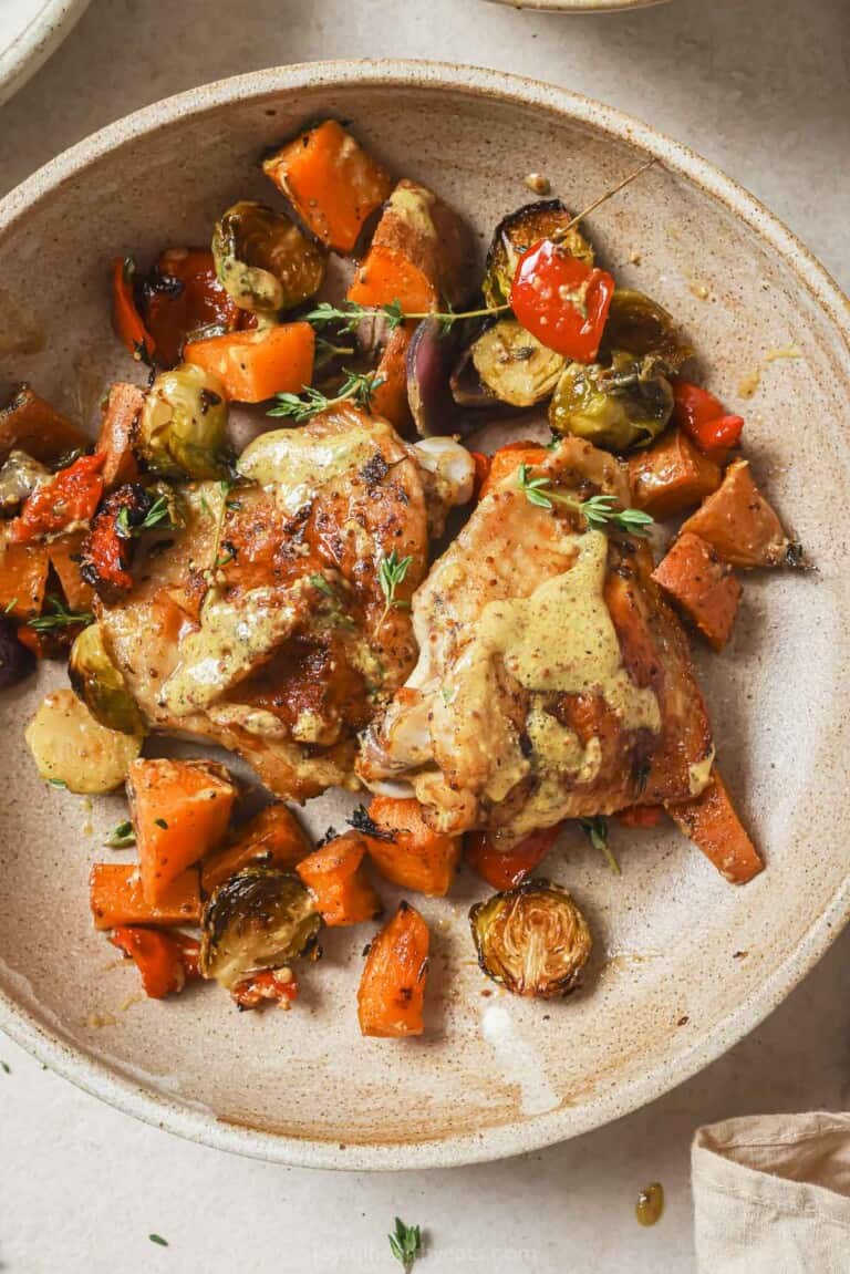 Sheet pan chicken thighs with extra honey mustard sauce in a bowl.