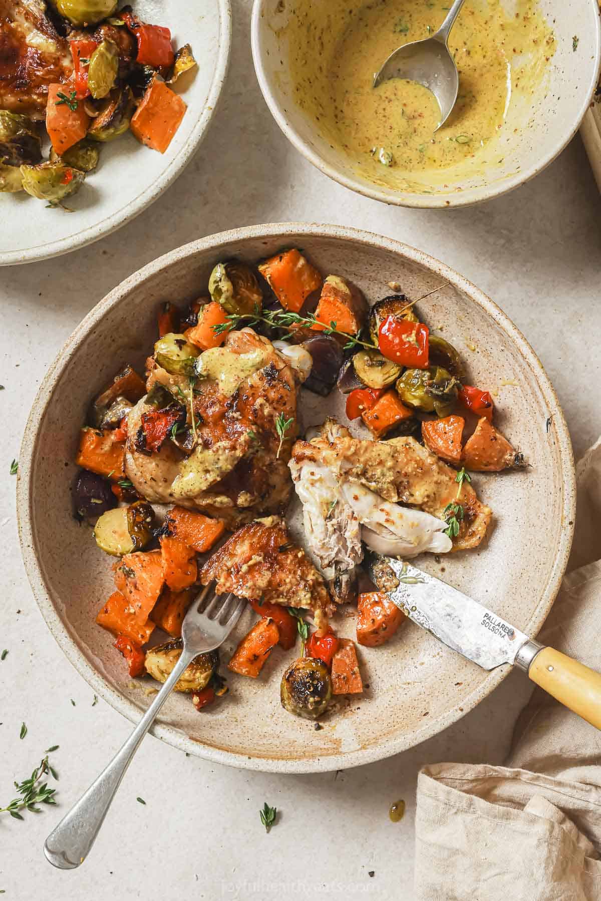 Cutting into the baked sheet pan chicken thighs with veggies on a plate. 