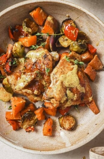 Sheet pan chicken thighs with extra honey mustard sauce in a bowl.