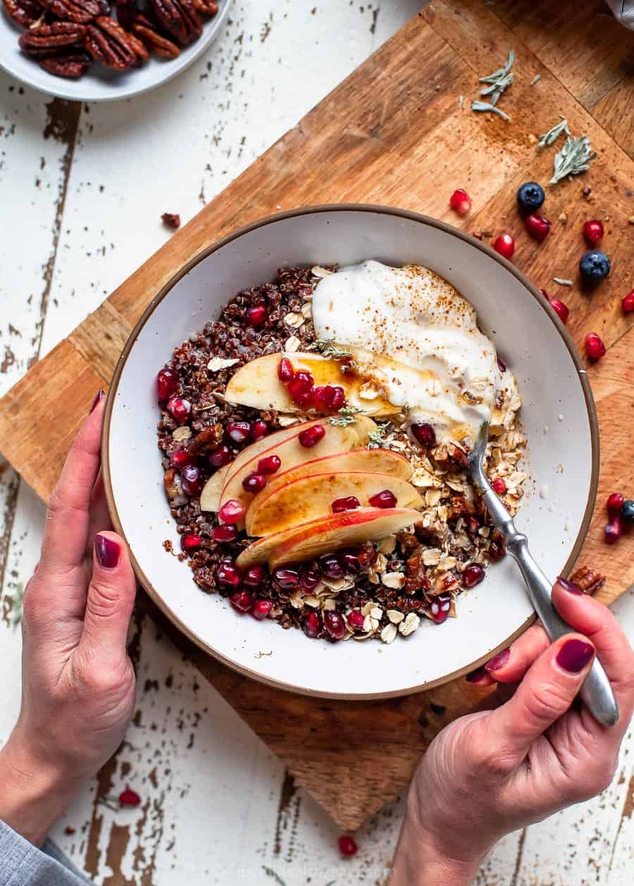 overhead photo of apple cinnamon breakfast grain bowl with hands holding the bowl