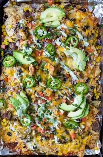The Ultimate Cheesy Sheet Pan Steak Nachos with layers of cheese, steak, veggies and a drizzle of cilantro lime crema. These epic nachos make the perfect fun weeknight dinner or game day appetizer! #glutenfree