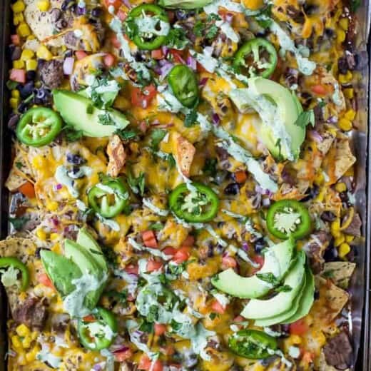 The Ultimate Cheesy Sheet Pan Steak Nachos with layers of cheese, steak, veggies and a drizzle of cilantro lime crema. These epic nachos make the perfect fun weeknight dinner or game day appetizer! #glutenfree