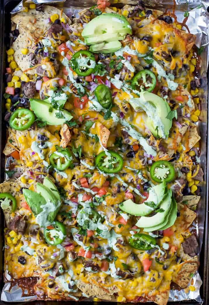 Loaded nachos on a baking sheet with melted cheese and fixings.