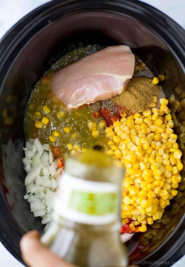 This healthy white chicken chili recipe is filled with juicy chicken, hearty pinto beans, tender corn, and more. Perfect for chilly days! Top view of ingredients for white chicken chili in a crockpot.