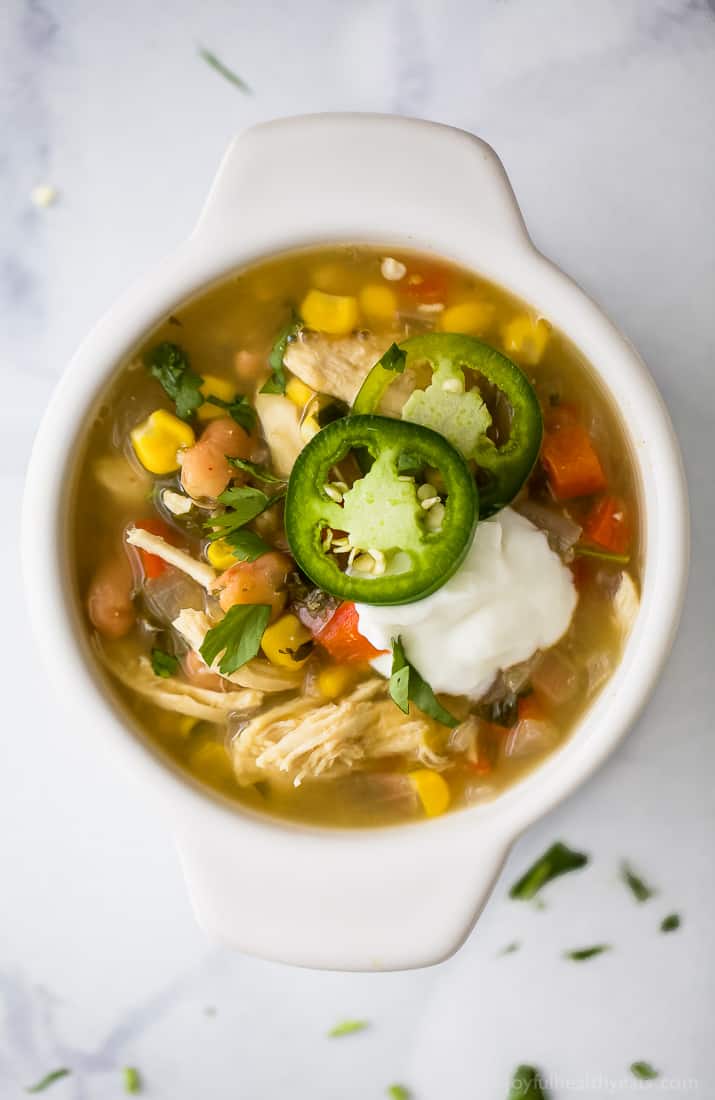 Top view of a bowl of white chicken chili with jalapeno slices and sour cream.