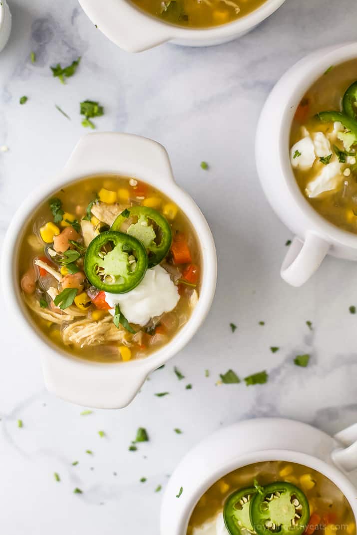 Top view of crocks of white chicken chili with jalapeno slices and sour cream.