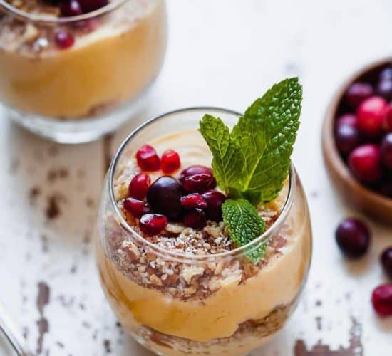 A pumpkin pie parfait on a chipped white table beside a metal spoon