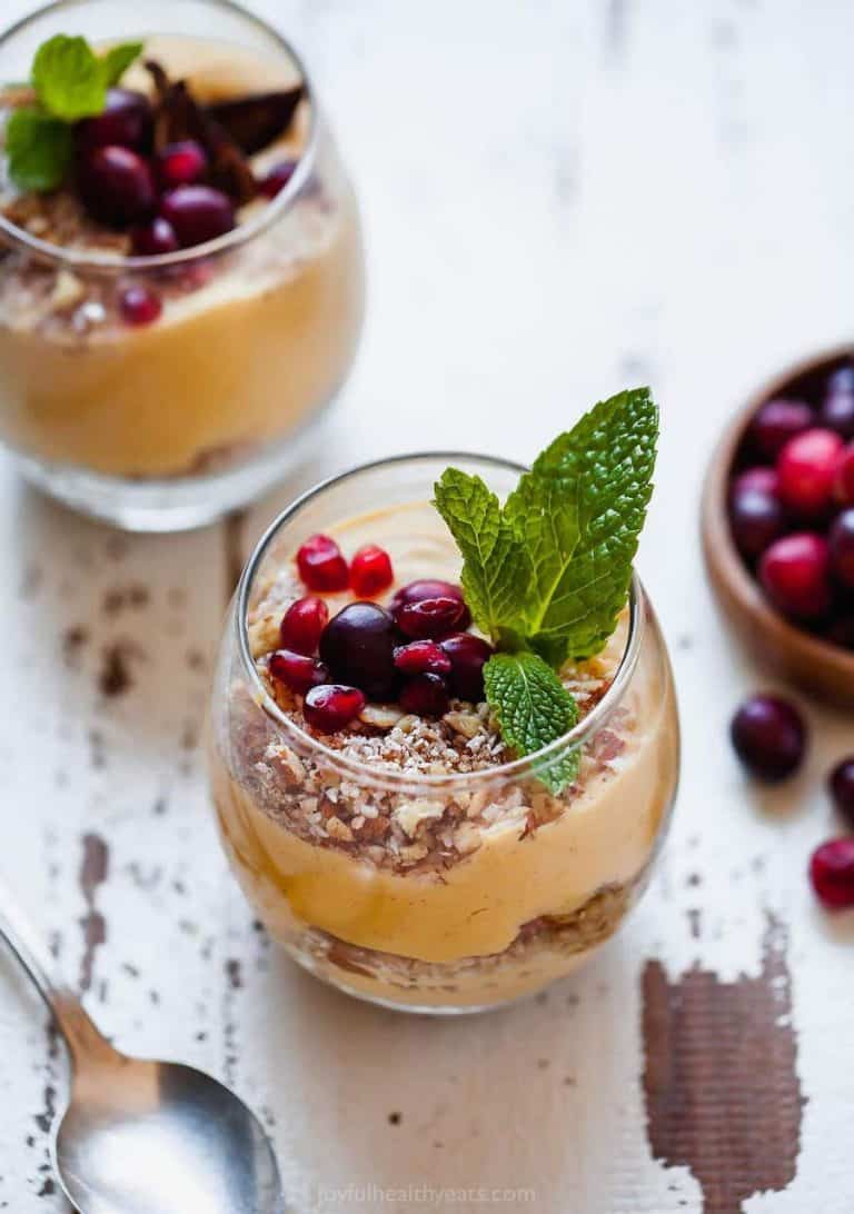 A pumpkin pie parfait on a chipped white table next to a metal spoon