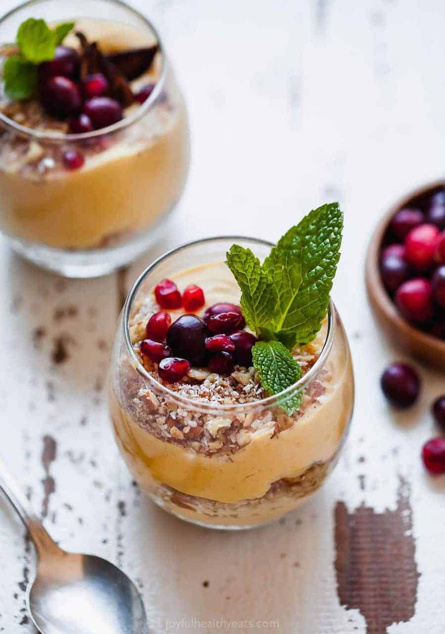 A pumpkin pie parfait on a chipped white table beside a metal spoon