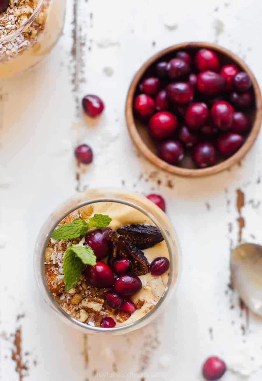 A parfait next to a bowl of cranberries shown from the top