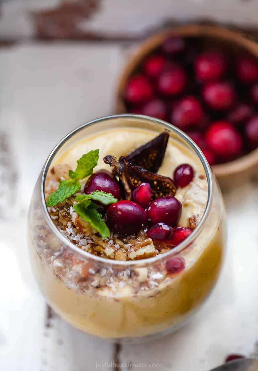 A close-up shot of a homemade parfait in a drinking glass with a bowl of cranberries behind it