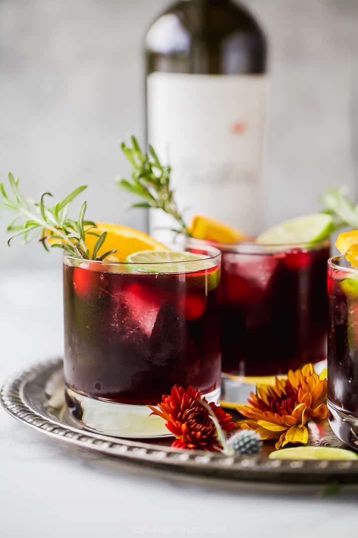 Glasses of Thanksgiving holiday sangria garnished with citrus slices and rosemary sprigs served on a metal tray.