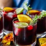 Glasses of Thanksgiving holiday sangria garnished with citrus slices and rosemary sprigs served on a metal tray.