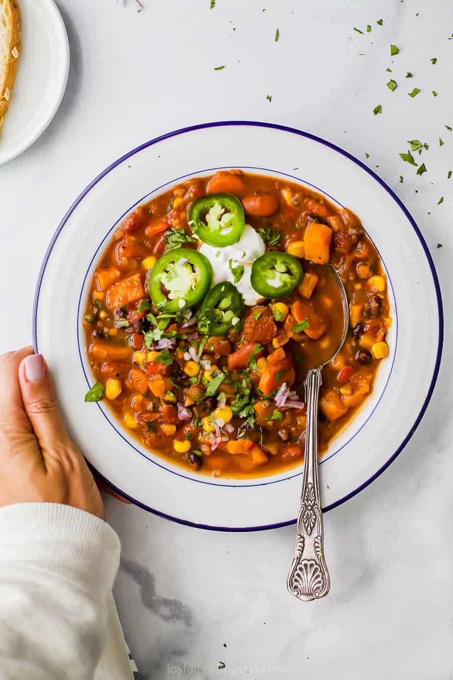 This sweet potato black bean chili is an easy Instant Pot vegetarian chili recipe made with corn, carrots, two kinds of beans, and more! Bowl of instant pot sweet potato black bean chili with a hand holding the bowl.
