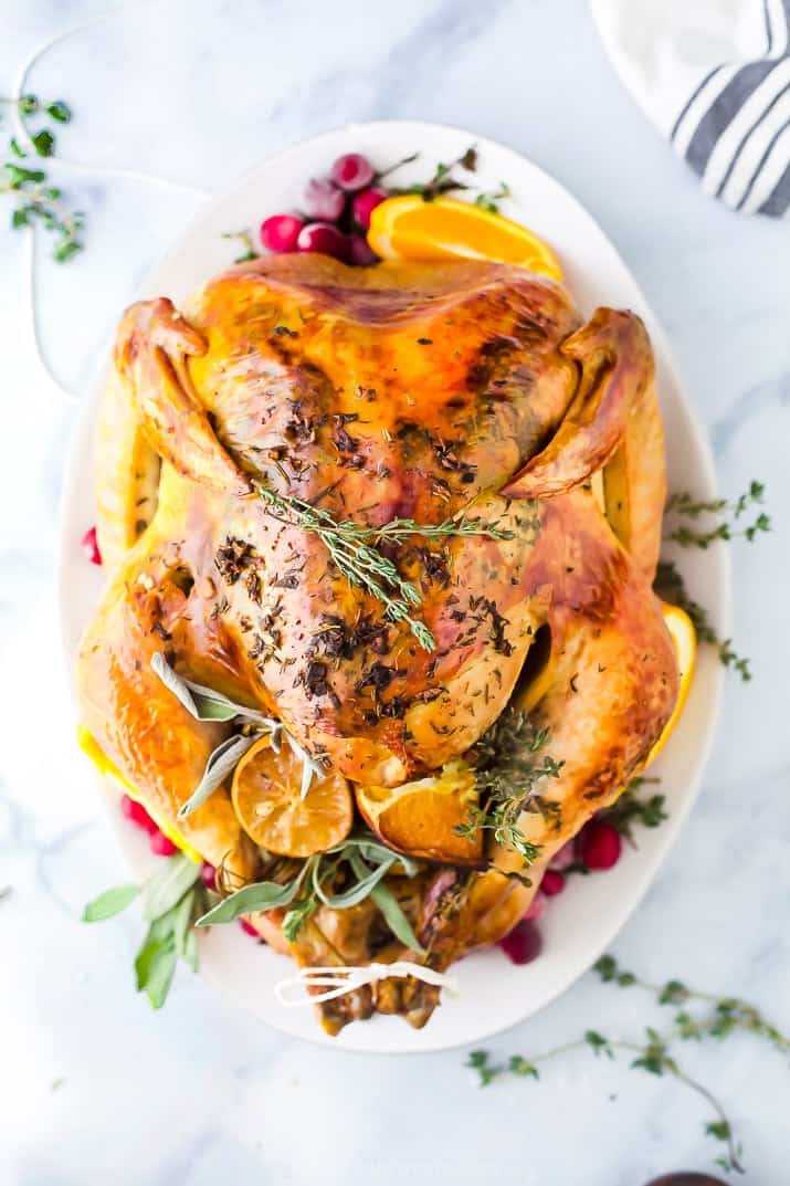 Cooked Thanksgiving turkey on a white platter garnished with cranberries and herbs