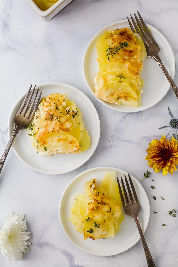 Three plates with forks and a serving of cheesy scalloped potatoes on top of a granite surface