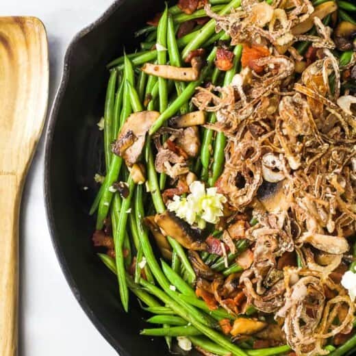 Healthy green bean casserole in a skillet near a wooden spoon.