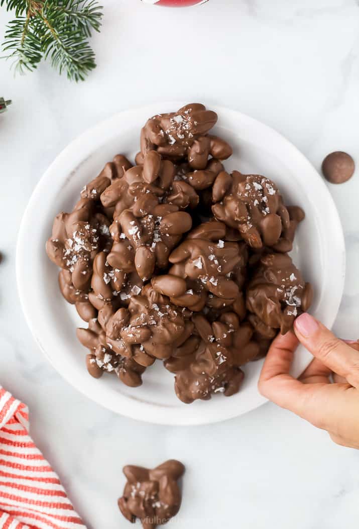 photo a hand grabbing Sweet & Salty Chocolate Toasted Almond Clusters on a plate