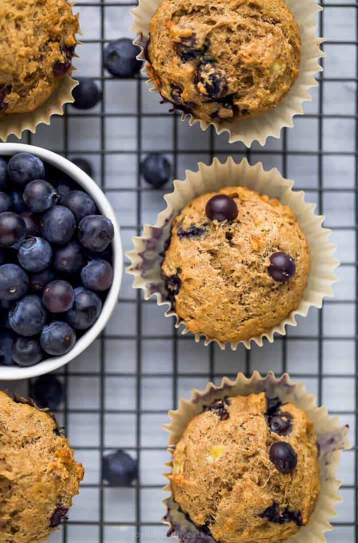 picture of healthy banana blueberry muffins on a cooling rack with a bowl of blueberries