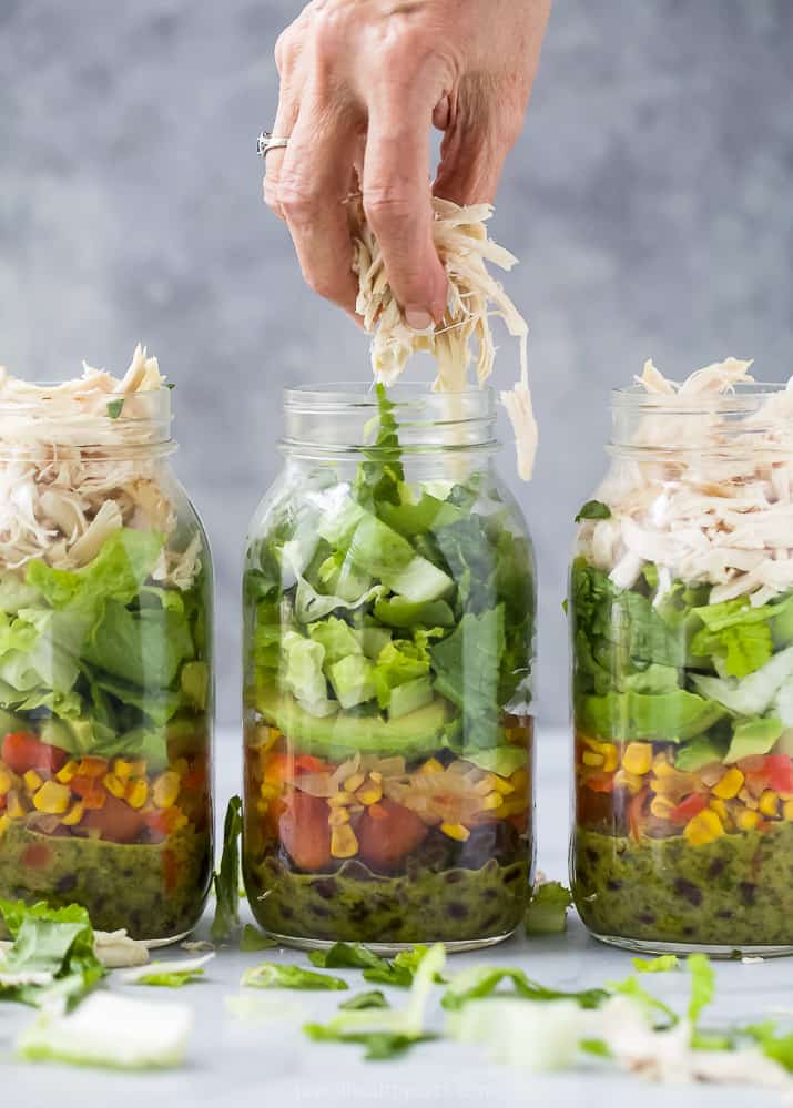 putting rotisserie chicken on top of Mason Jar Southwest Chicken Salad with Cilantro Lime Dressing