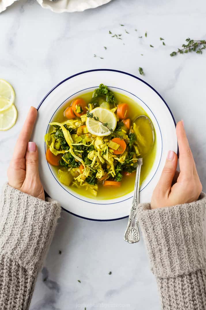 healing chicken soup recipe served in a bowl with hands holding the bowl