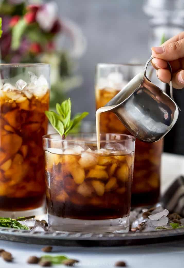 pour coconut milk creamer into thai iced coffee in a glass with mint