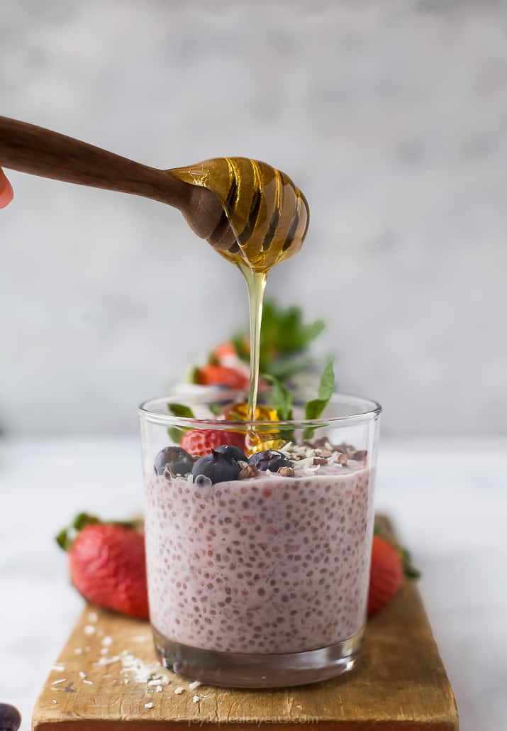 honey being drizzled on top of a jar filled with strawberry chia pudding