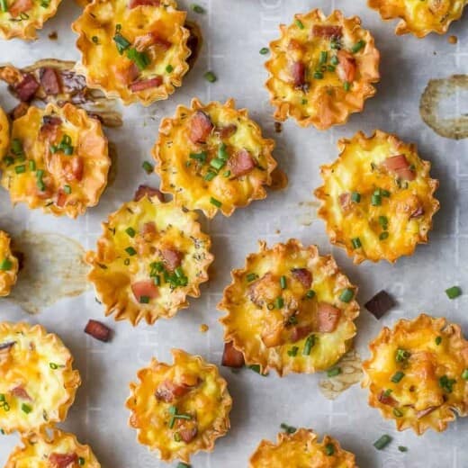 ham and cheese mini quiches topped with chives on parchment paper