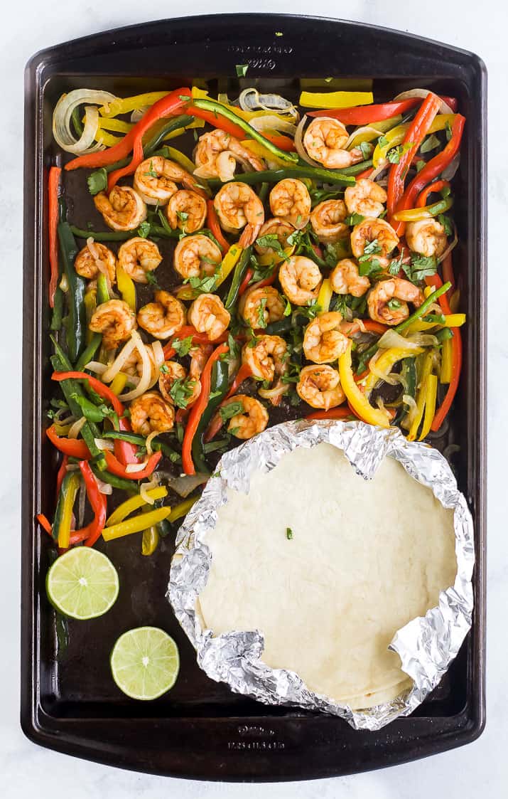 finished product of sheet pan shrimp fajitas on a baking sheet with tortillas