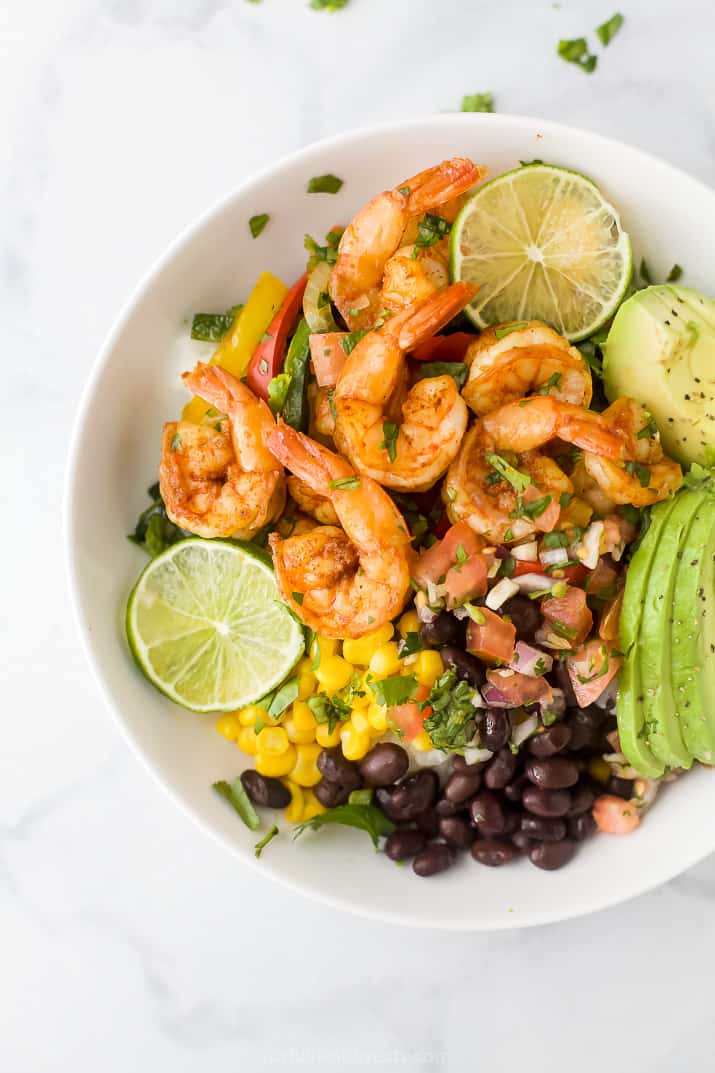 sheet pan shrimp fajitas in a rice bowl with avocado, corn and pico de gallo