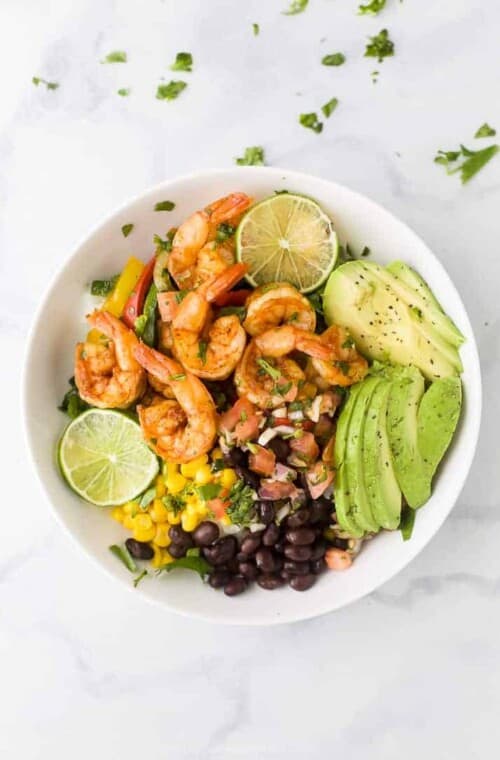 Bowl of spicy shrimp sheet pan fajitas with sliced avocado, black beans, corn, and pico de gallo.