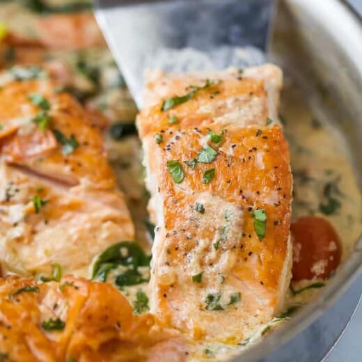 a spatula scooping creamy tuscan pan seared salmon in a skillet