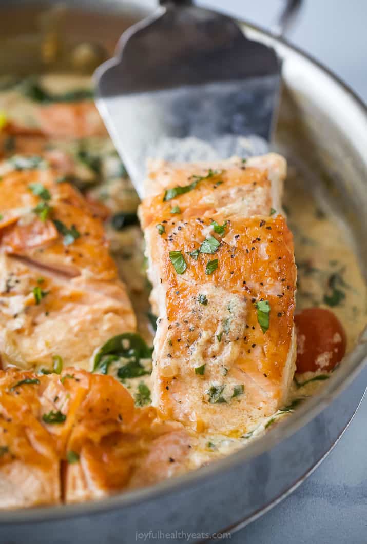 a spatula scooping creamy tuscan pan seared salmon in a skillet