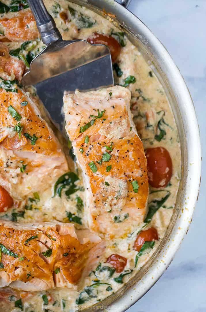 creamy tuscan pan seared salmon in a skillet with a spatula underneath