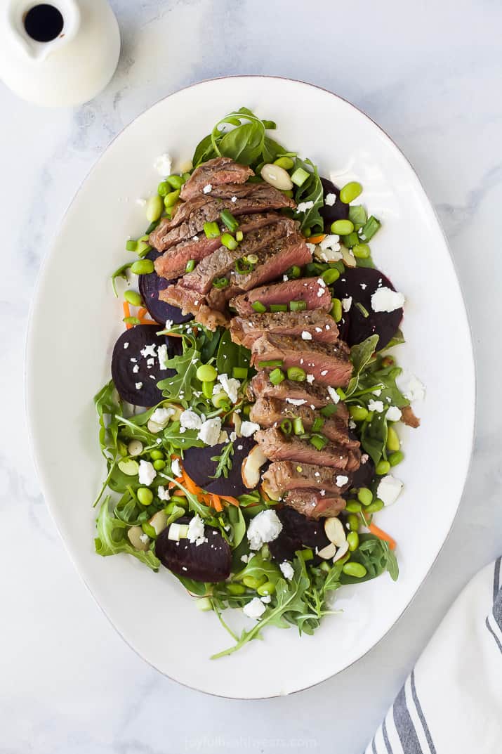 a large plate filled with roasted beet steak salad topped with goat cheese and balsamic vinaigrette