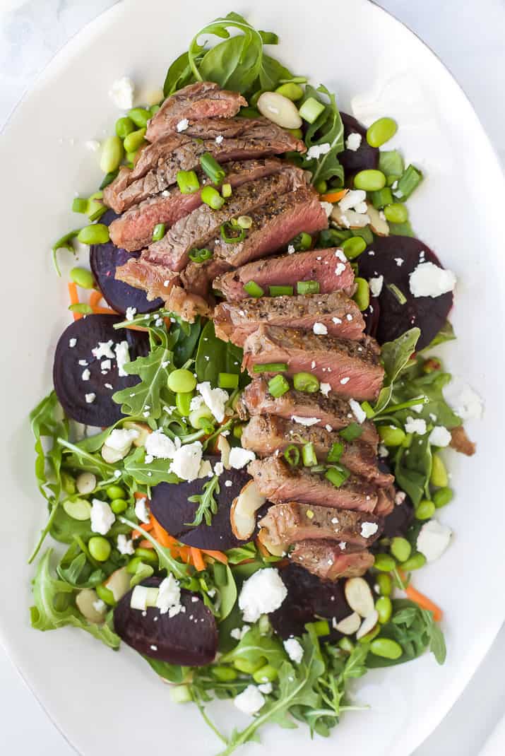 large plate filled with roasted beet steak salad topped with goat cheese