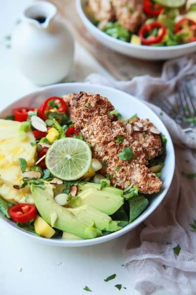 coconut almond crusted chicken tenders in a salad with avocado, mango, red pepper and drizzled with honey dijon dressing