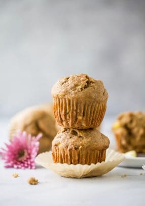 A stack of two whole wheat banana muffins on a countertop with a pink flower beside them