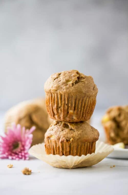 A stack of two whole wheat banana muffins on a countertop with a pink flower beside them