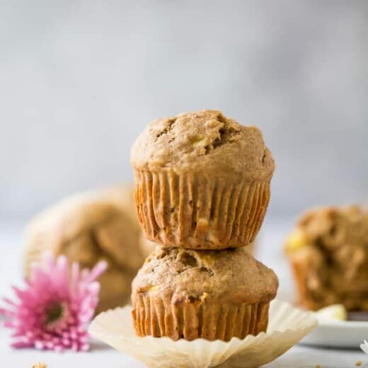 A stack of two whole wheat banana muffins on a countertop with a pink flower beside them