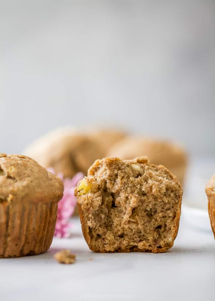 A halved muffin on a countertop with more banana muffins beside it