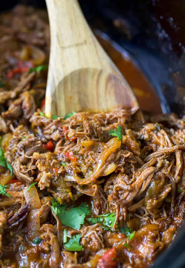 ropa vieja recipe (cuban shredded beef) in a crock pot with a spoon scooping the beef